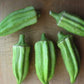 five small fat green okra pods arranged on a wooden table