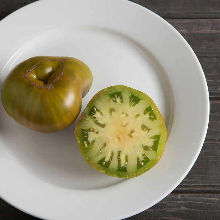A large whole tomato with streaks of green and orange, and a another half tomato showing pale green inside flesh, arranged on a white plate